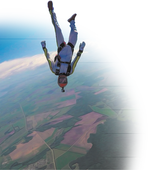 Fotografia de um homem de ponta cabeça em um salto livre. O homem está usando roupas e equipamentos para o salto, incluindo macacão, luvas e capacete. Atrás do homem há uma nuvem e no solo há regiões com vegetação e terra.