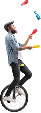 Fotografia de um homem usando boina, camisa e calça jeans sobre um monociclo e fazendo malabarismo, com pinos de plástico colorido. Dois pinos estão no ar enquanto ele segura outros dois.