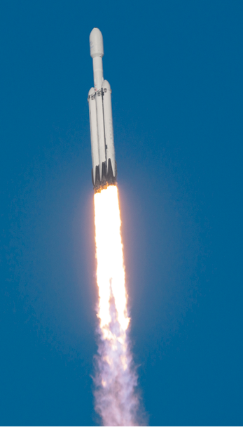 Fotografia de um foguete em lançamento no céu. O foguete tem estrutura alongada e branca. Na parte inferior há labaredas de fogo saindo do foguete.