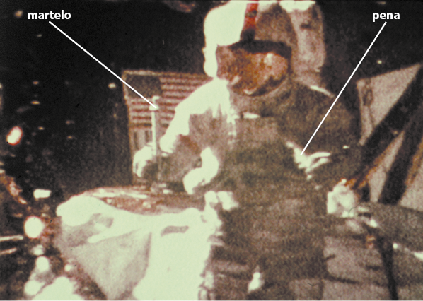 Fotografia de um astronauta no espaço, segurando um martelo com uma mão e uma pena em outra mão.