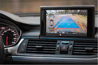 Fotografia de parte do painel de um carro, com um monitor no centro projetando na tela a câmera de ré acionada.