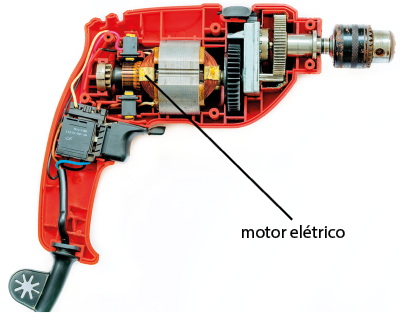 Fotografia da parte interna de uma furadeira. No meio dela há uma peça dourada denominada motor elétrico. Nas laterais há vária peças metálicas e alguns fios.