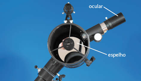 Fotografia de parte de um telescópio refletor. Ele possui uma parte cilíndrica, a qual dentro há um espelho circular. Acoplado nessa parte cilíndrica, há outro cilindro menor, em que a extremidade está indicada como ocular.