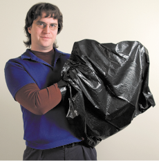 Fotografia de um rapaz com as mãos dentro de um saco preto. Ele tem cabelos com franja e usa óculos com lente transparente.