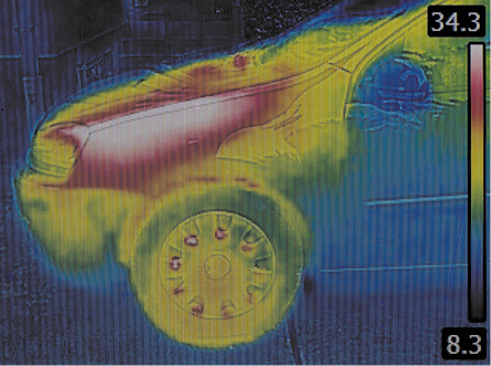 Fotografia com câmera infravermelha da parte frontal de um carro em um sensor de calor. A região do motor está na cor branca com contorno vermelho. As partes do carro próximas a essa região, estão em amarelo e verde e o restante está em azul. No lado direito há uma faixa vertical com uma escala de cores indicando a temperatura, de baixo para cima, a temperatura mais fria 8,3 em azul escuro, azul claro, verde, amarelo, vermelho e branco, a temperatura mais quente 34,3.