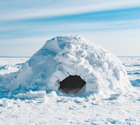 Fotografia de um iglu construído com blocos de neve. Ao fundo, o céu está claro e com algumas nuvens.