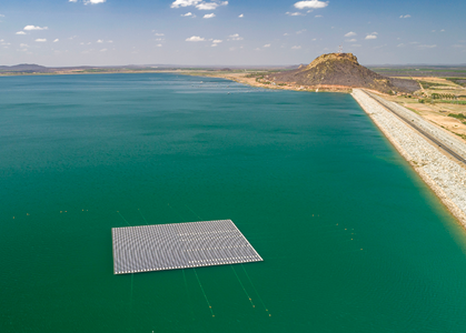 Fotografia de parte de uma represa. Sobre a água que tem coloração verde há uma placa de captação de energia solar em formato retangular.