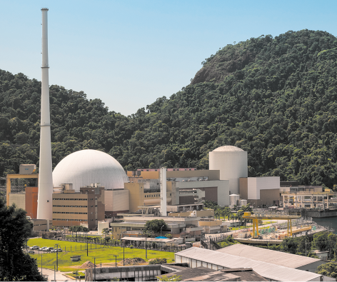 Fotografia de uma usina nuclear. Há várias construções, uma delas tem formato esférico e algumas torres. Ao fundo há montanhas com vegetação.