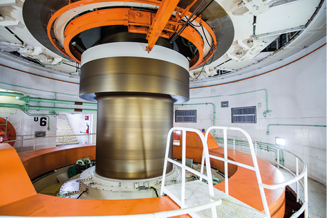 Fotografia de uma grande turbina de metal com formato cilíndrico no meio de uma sala com formato circular.