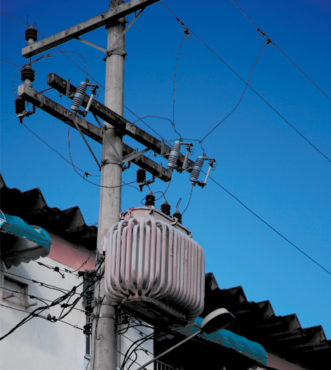 Fotografia de um poste de rede elétrica em frente a uma casa.