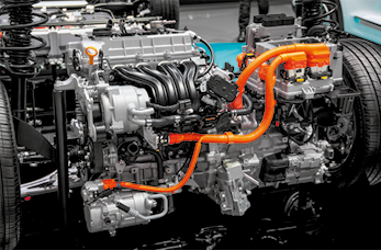 Fotografia de um motor de um automóvel formado por várias peças de metal, fios e canos. Nas laterais há um pneu de cada lado.