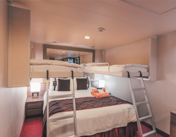 Fotografia de um pequeno quarto, com cama de casal, um pequeno armário de cada lado del. E há duas escadas indo para camas suspensas.
