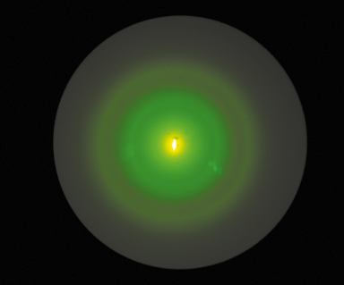 Ilustração de uma mancha circular, com degradê indo para um verde interno. No centro há um pequeno objeto oval amarelo iluminado.