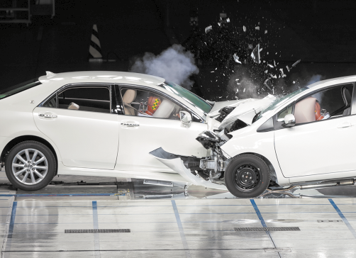 Fotografia de uma colisão frontal entre dois carros, com as partes dianteiras destruídas e, dentro, os airbag acionados e bonecos com as cabeças apoiadas nesses dispositivos.