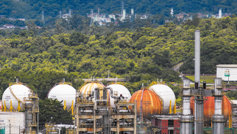 Fotografia de vários tanques esféricos e próximos de algumas torres. Ao fundo há uma área de mata fechada.