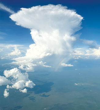 Fotografia com vista aérea do céu azul claro com uma grande nuvem branca e alta. Ao lado há nuvens menores.