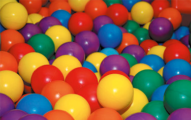 Fotografia de várias bolinhas de plástico coloridas e misturadas. Há bolinhas amarelas, laranjas, vermelhas, azuis, verdes e roxas.