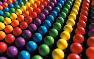 Fotografia de várias bolinhas de plástico coloridas e enfileiradas. Cada fila é formada por bolinhas de uma só cor. Há filas de bolinhas amarelas, laranjas, vermelhas, azuis, verdes e roxas.