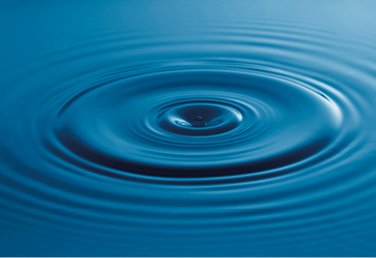 Fotografia de uma gota em uma superfície d’água. Em torno da gota há várias ondas em formato de círculos.