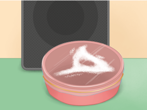 Ilustração de um recipiente redondo coberto por filme de P V C. E em cima há um pó branco formando uma figura com três pontas e um buraco no centro. Atrás do recipiente há uma grande caixa de som.