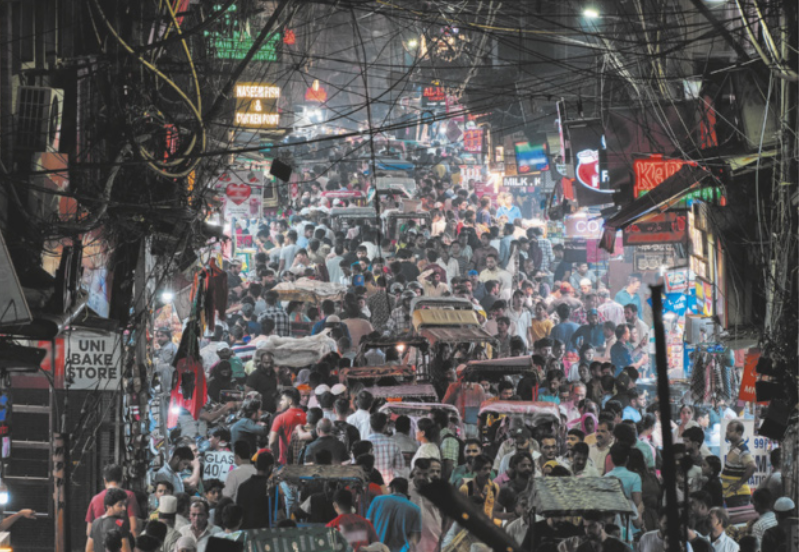 Foto de muitas pessoas e carros se deslocando pela rua.