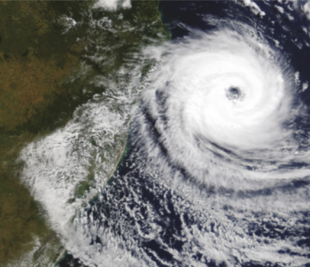 Foto aérea de um furacão. Ele se aproxima do continente e é formado por nuvens que se movem em espiral. No centro, há uma espécie de abertura.