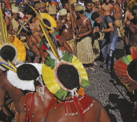Foto de homens indígenas em manifestação. Eles usam cocares, colares e carregam chocalhos.