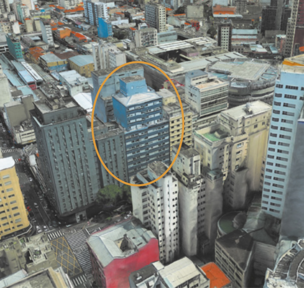 Foto de edifício azul, situado no meio de dois outros edifícios.