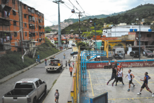 Foto de uma rua com prédios na lateral. Do outro lado da rua, encontra-se uma quadra.