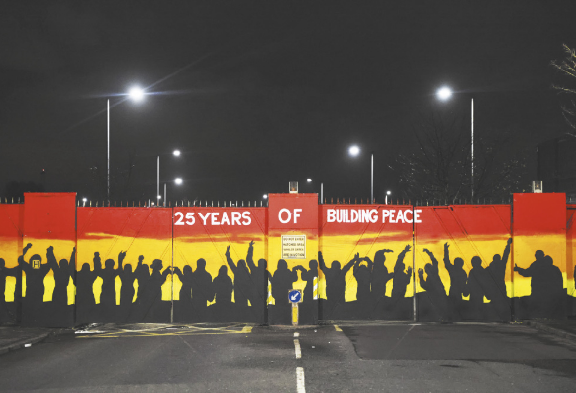 Mural que apresenta a sombra de muitas pessoas reunidas e as seguintes inscrições em inglês: 'Há 25 anos construindo a paz'.