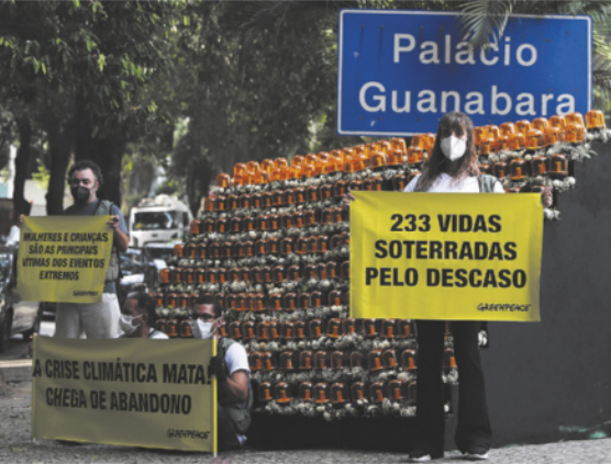 Foto de pessoas em protesto. Elas seguram cartazes, onde está escrito '233 vidas soterradas pelo descaso', 'A crise climática mata, chega de abandono', 'Mulheres e crianças são as principais vítimas dos eventos extremos'.