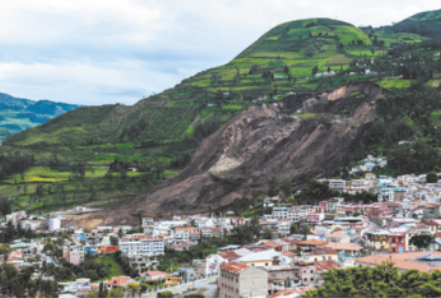 Foto de deslizamento de terra em área inclinada. É possível identificar terra acumulada ao lado das casas instaladas em locais mais baixos.