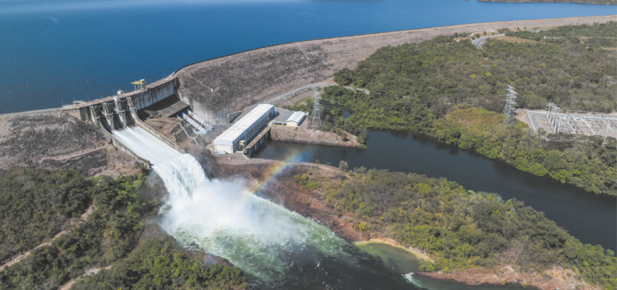 Foto de Usina Hidrelétrica, localizada em um terreno com desnível. Há muita água represada na área mais alta. Essa água desce por meio de grandes tubulações, chegando à parte inferior do terreno.