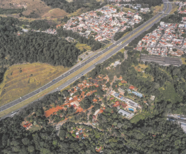 Foto aérea que apresenta, em primeiro plano, uma comunidade integrada ao espaço natural do entorno. Ao fundo, destaca-se uma estrada e uma cidade.