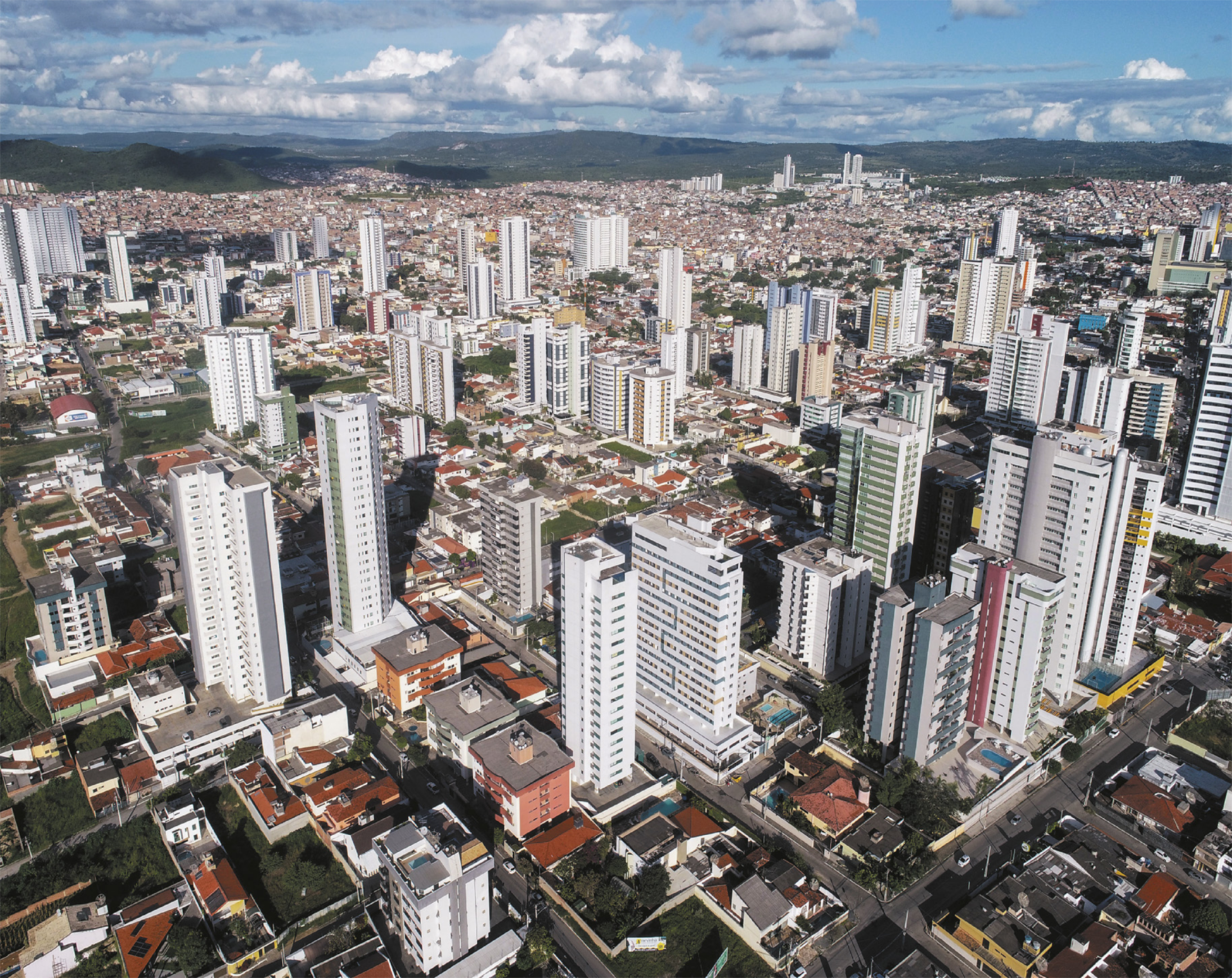Foto aérea de uma cidade. Destacam-se muitos prédios altos, casas, ruas e algumas áreas de parque.