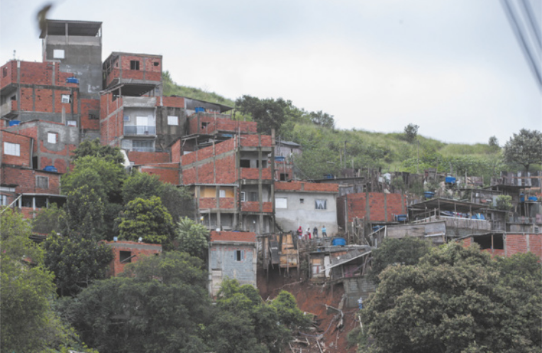 Foto de moradias, construídas em local inclinado. Essas casas possuem os tijolos e a estrutura expostos.