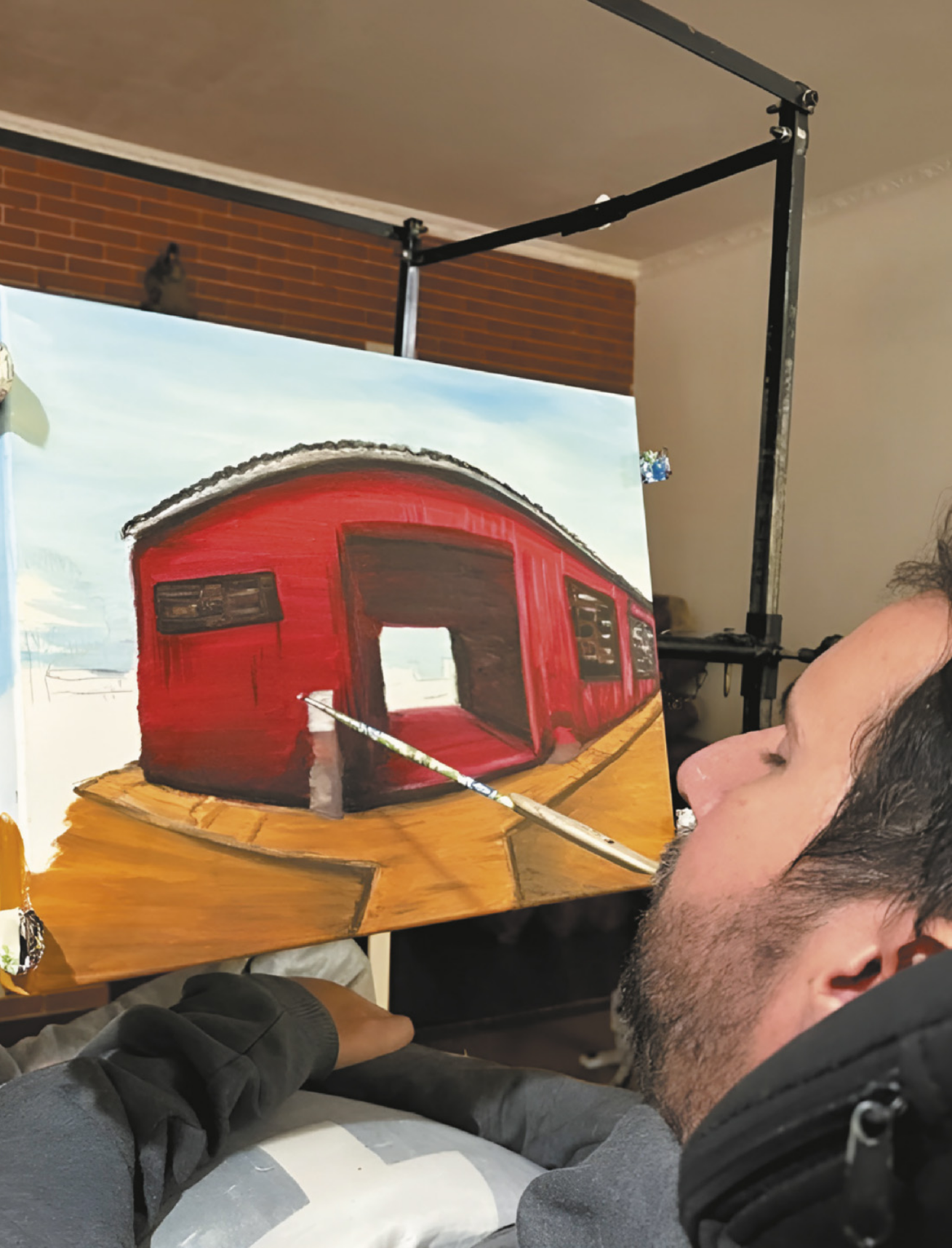 Foto de homem pintando um quadro. Ele segura o pincel com a boca.