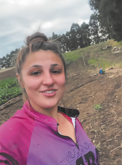 Foto de jovem branca. Ela tira uma foto de si mesma junto a uma área de plantação.