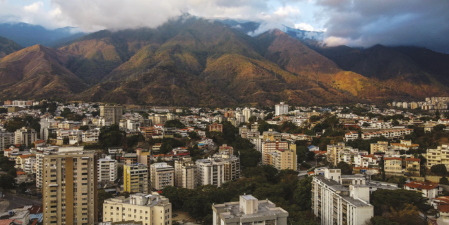 Foto de cidade instalada ao lado de grandes montanhas. Destacam-se muitos prédios e casas.