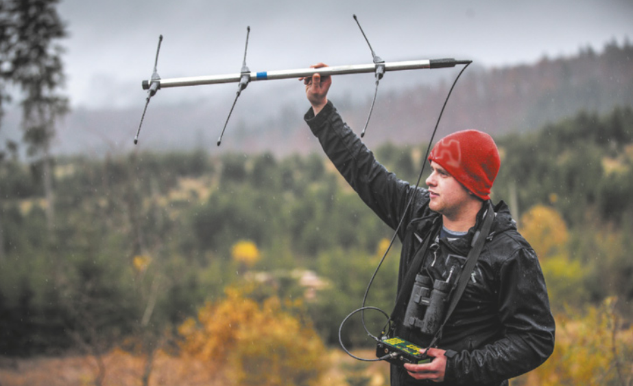 Foto de homem posicionando uma antena no alto. Essa antena está presa a um pequeno equipamento.