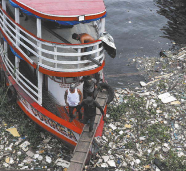 Foto de pessoas desembarcando de um navio. Esse navio está em um rio muito poluído. Destacam-se embalagens e objetos boiando na água.