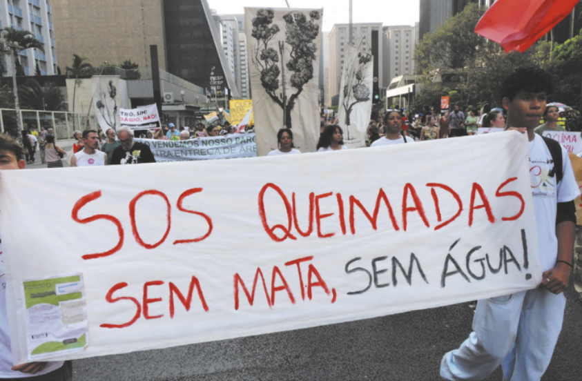 Foto de pessoas em manifestação. Eles seguram uma faixa, onde está escrito 'S O S queimadas. Sem mata, sem água!'.