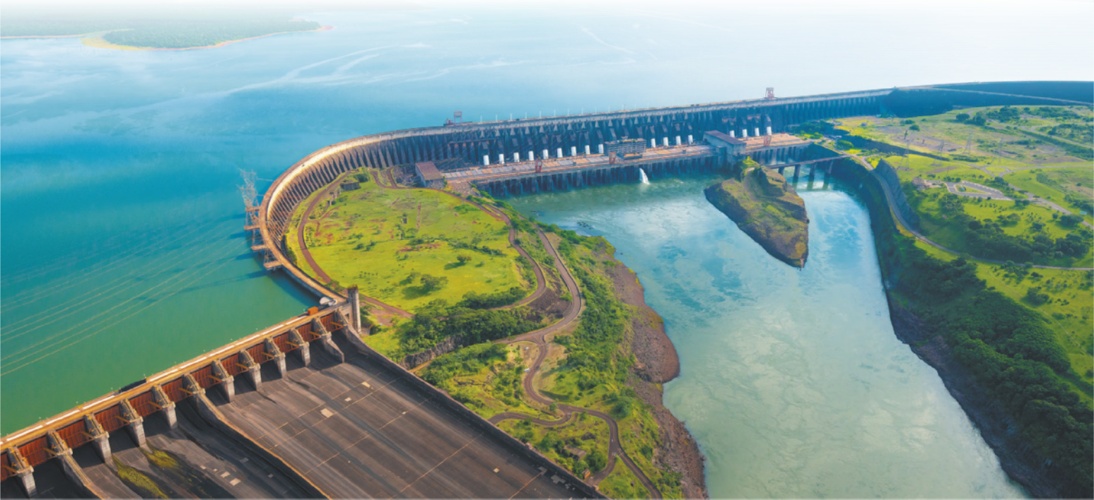Foto de Usina Hidroelétrica, localizada em um terreno com desnível. Há muita água represada na área mais alta. Essa água desce por meio de grandes tubulações, chegando à parte inferior do terreno.