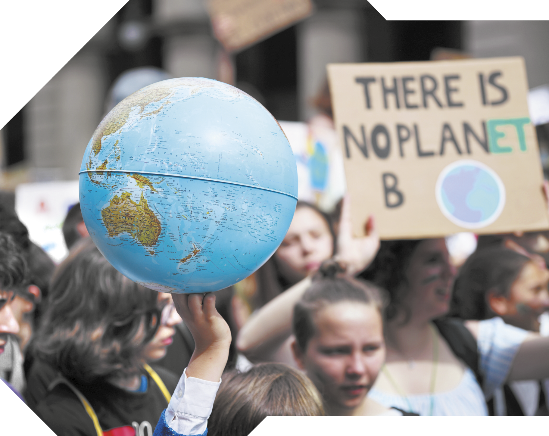 Fotografia de uma manifestação com onde várias pessoas segurando cartazes. Em destaque, uma pessoa está com a mão levantada segurando um globo terrestre. Ao lado, outra pessoa segura um cartaz com a frase em inglês: THERE IS NO PLANET B.