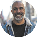 Fotografia de busto de um homem sorrindo. Ele é calvo, tem barba grisalha, e usa uma jaqueta jeans com forro de lã com uma camiseta escura por baixo.