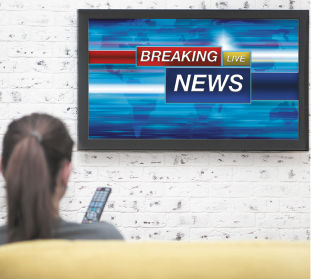 Fotografia de uma pessoa vista de costas assistindo TV. Na tela há o texto em inglês: BREAKING live NEWS.