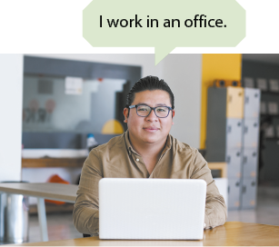 Fotografia de um homem de óculos e camisa de manga longa sentado de frente para um laptop aberto em uma sala com mesa e armários. Há um balão de fala escrito em inglês: I work in an office.