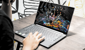 Fotografia de uma pessoa com a mão sobreposta no teclado de um laptop que está sobre uma mesa.