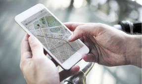 Fotografia de uma pessoa segurando um smartphone com um mapa com uma rota sendo exibida na tela.