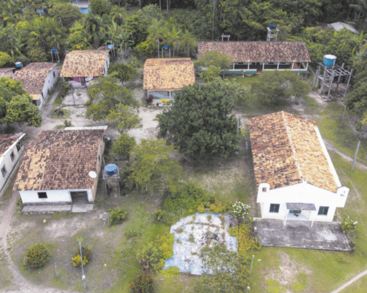 Fotografia aérea de uma comunidade quilombola, construída em meio a uma área de vegetação abundante, com várias árvores e plantas. As construções são simples, feitas com paredes de alvenaria e cobertas com telhas cerâmicas.
